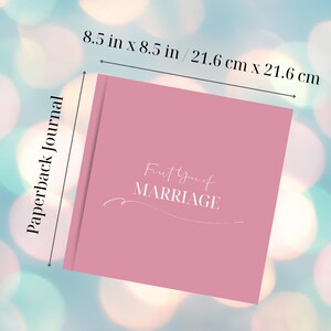 Puede incluir: Un diario de bolsillo rosa con el texto "First Year of Marriage" en escritura blanca. El diario mide 21,6 cm por 21,6 cm. Las palabras "Paperback Journal" est&aacute;n impresas verticalmente en el lado izquierdo del diario.