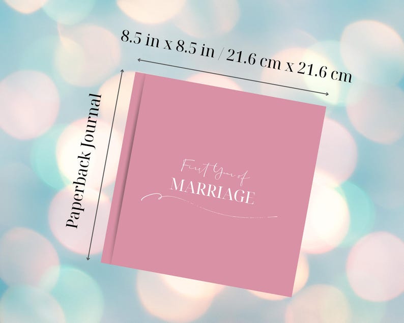 Puede incluir: Un diario de bolsillo rosa con el texto "First Year of Marriage" en escritura blanca. El diario mide 21,6 cm por 21,6 cm. Las palabras "Paperback Journal" est&aacute;n impresas verticalmente en el lado izquierdo del diario.
