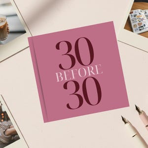 May include: A pink journal with the text "30 BEFORE 30" in dark burgundy and white. The journal is surrounded by polaroid-style photos, pens, and a glass of iced coffee. The image suggests a lifestyle and planning theme.