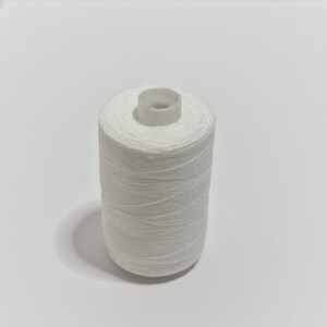 May include: A spool of white thread, tightly wound around a white plastic core. The thread is a bright white color, and the spool is cylindrical. The image is taken against a plain white background.
