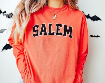 May include: Coral long-sleeve shirt with the word "SALEM" in black block letters. The shirt has a classic crew neck and a relaxed fit. The shirt is a comfortable and stylish option for casual wear.