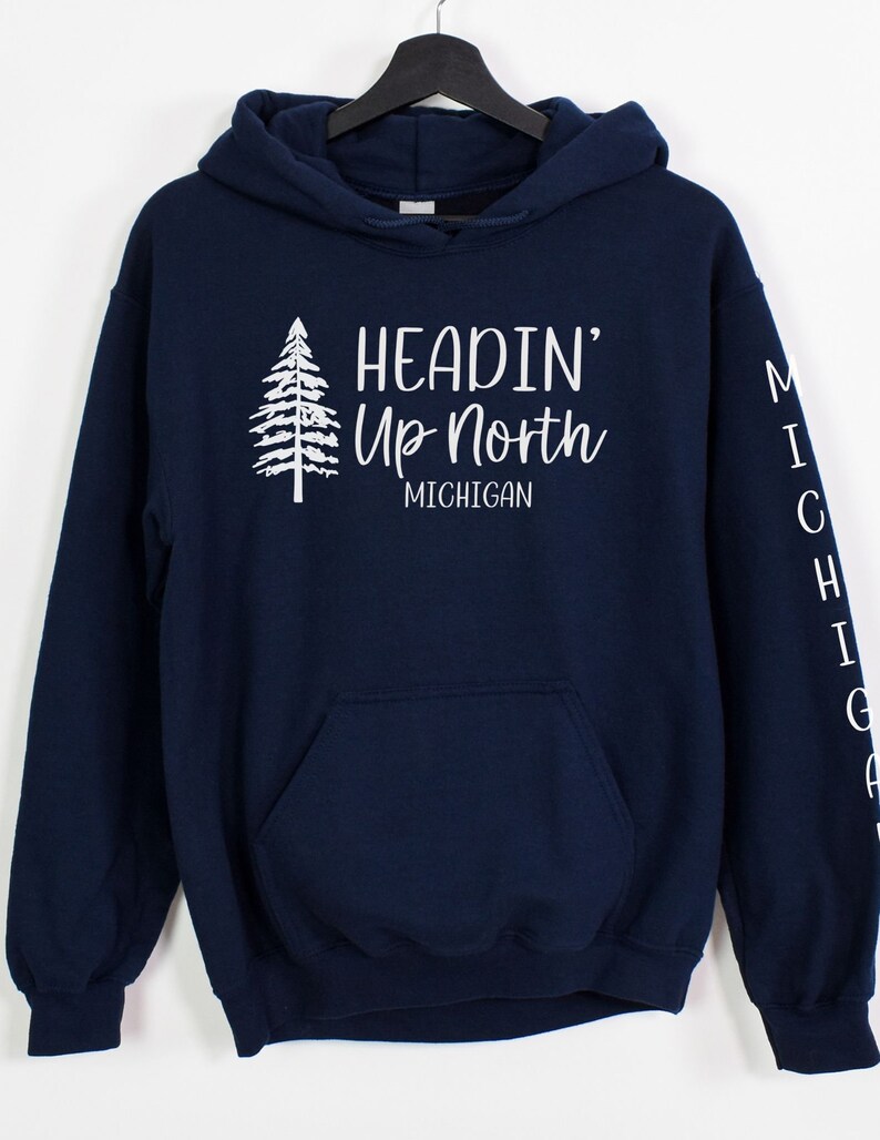 May include: Navy blue hooded sweatshirt with a white graphic of a pine tree and the text "Headin' Up North Michigan". The left sleeve has the word "Michigan" vertically down the sleeve.