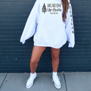 May include: A gray hoodie with the text "Headin' Up North Michigan" and a pine tree graphic on the front. The word "Michigan" is written vertically down the left sleeve.
