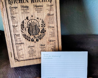 May include: A rectangular wooden board engraved with the title Kitchen Witchery and a list of herbs categorised by intent, featuring a central cauldron illustration. A matching wooden stand with moon phase carvings holds a lined recipe card.