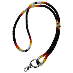 May include: A beaded lanyard with a silver and black beaded design. The lanyard has a silver and black beaded design with red, yellow, and white accents. The lanyard has a silver clip and a silver ring.
