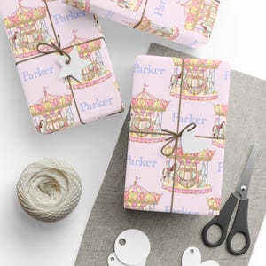 May include: Pink wrapping paper featuring a carousel pattern, tied with brown twine and a star-shaped tag. The word "Parker" is printed on the paper. A ball of twine, scissors, and blank tags are also present.