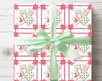May include: Gift-wrapped present with a white background featuring a repeating pattern of playing cards, red crosshatch lines, and a green satin bow. The playing cards include a bird illustration and the word "Joker".