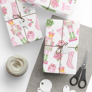 Può includere: Regali confezionati con motivi festivi rosa e verdi, tra cui schiaccianoci, fiocchi e stelle di Natale. I regali sono legati con spago e adornati con etichette a forma di cuore. Sono presenti anche un gomitolo di spago, forbici ed etichette vuote.