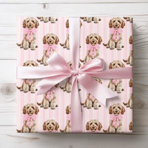 May include: Gift-wrapped present featuring a repeating pattern of a dog wearing a pink bow on pink striped wrapping paper. A large pink satin ribbon and bow are tied around the gift. The dog has brown fur and is sitting upright.
