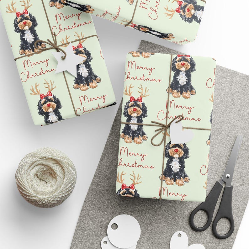 May include: Gift-wrapped presents with light green paper featuring a repeating pattern of a black and brown dog wearing a red bow and antlers. The words "Merry Christmas" are printed in red. The gifts are tied with twine and adorned with white star-shaped tags.