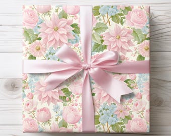 May include: A wrapped gift box featuring a floral pattern of pink poinsettias, roses, and blue hydrangeas on a cream background. A light pink satin ribbon is tied in a bow around the box, creating a decorative and elegant presentation.