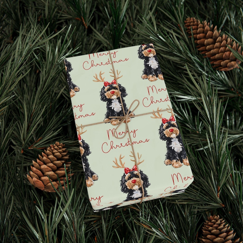 May include: A wrapped gift with a light green background featuring a repeating pattern of a black and white dog wearing reindeer antlers and a red bow. The words "Merry Christmas" are written in red. The gift is tied with twine.
