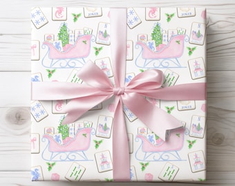 May include: A wrapped gift with a light pink satin bow. The wrapping paper features a repeating pattern of pink sleighs, Christmas trees, playing cards, and holly on a white background. The bow is tied in a classic style.