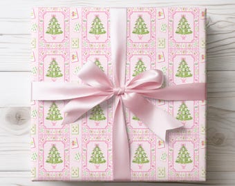 May include: A wrapped gift with pink wrapping paper featuring a repeating pattern of green Christmas trees and playing cards on a pink background. A light pink satin ribbon is tied in a bow around the gift.