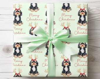 Puede incluir: Regalo envuelto con papel de regalo verde claro con un patrón repetido de perros negros, blancos y marrones con lazos rojos y cornamentas, con las palabras "Merry Christmas" en rojo. Una cinta de raso verde claro está atada alrededor del regalo.