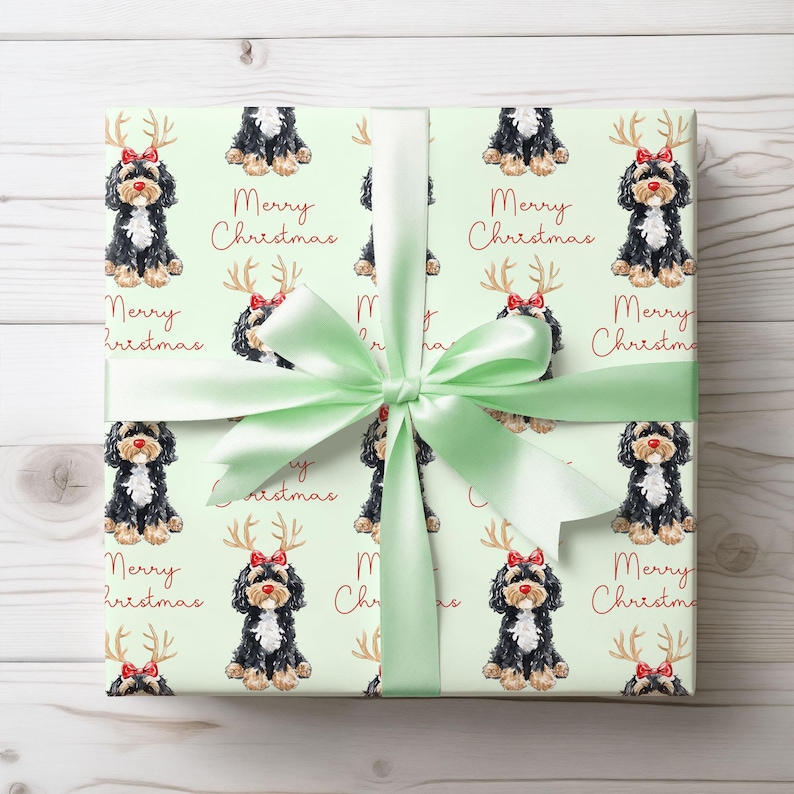 May include: Wrapped gift with light green wrapping paper featuring a repeating pattern of black, white, and brown dogs wearing red bows and antlers, with the words "Merry Christmas" in red. A light green satin ribbon is tied around the gift.
