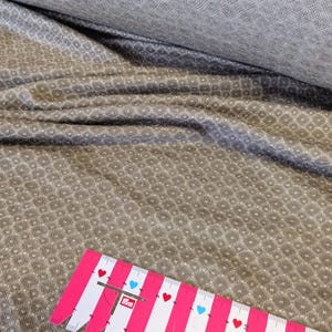 Könnte beinhalten: Nahaufnahme eines braunen Stoffes mit einem weißen geometrischen Muster. Ein rosa Lineal mit roten und blauen Herzen liegt auf dem Stoff.