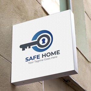 以下が含まれることがあります： 青い文字で「SAFE HOME」と書かれた白い正方形の看板。鍵のロゴがあり、鍵はグレーと青で、中央に鍵穴があります。看板は、質感のあるベージュ色の壁に取り付けられています。