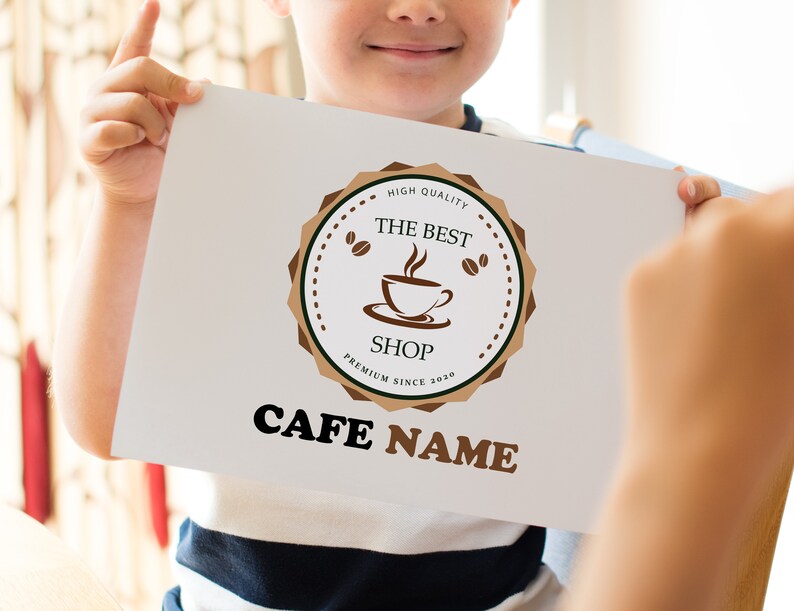May include: A white sign with a brown logo featuring a coffee cup and the text "The Best Shop" in a brown circle with the text "High Quality" and "Premium Since 2020" in smaller text. The text "Cafe Name" is below the logo in brown.