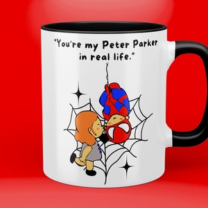 Puede incluir: Taza de cer&aacute;mica blanca con asa negra. La taza tiene una imagen de dibujos animados de una ni&ntilde;a besando a Spiderman en una telara&ntilde;a. El texto en la taza dice "You're my Peter Parker in real life."