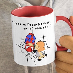 Puede incluir: Taza de cer&aacute;mica blanca con borde y asa rojos. La taza presenta una ilustraci&oacute;n de dibujos animados de Spider-Man colgando boca abajo de una telara&ntilde;a con una mujer de pie debajo. El texto en la taza dice "Eres mi Peter Parker en la vida real."