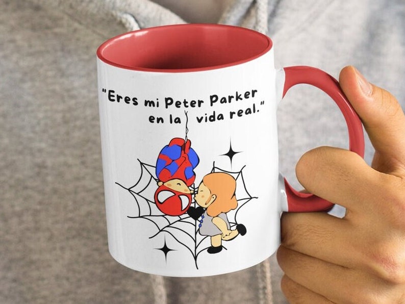 Puede incluir: Taza de cer&aacute;mica blanca con borde y asa rojos. La taza presenta una ilustraci&oacute;n de dibujos animados de Spider-Man colgando boca abajo de una telara&ntilde;a con una mujer de pie debajo. El texto en la taza dice "Eres mi Peter Parker en la vida real."