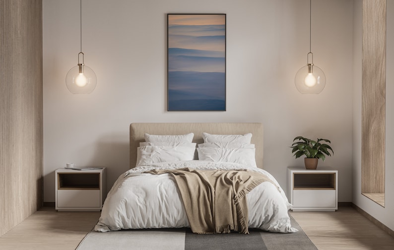 May include: A modern bedroom with a neutral color palette. The bed has white bedding and a tan throw blanket. Two bedside tables with lamps hang from the ceiling. A framed landscape art piece hangs above the bed. A potted plant sits on one of the bedside tables.