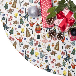 May include: White Christmas tree skirt with a Nutcracker theme. The skirt features a repeating pattern of Nutcracker soldiers, ballerinas, candy canes, presents, and other Christmas symbols. The skirt is decorated with red, blue, and gold accents.