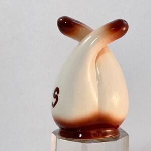 May include: A white ceramic salt and pepper shaker set shaped like two intertwined figures. The shakers have brown accents and the word "S" is visible on one of the shakers.