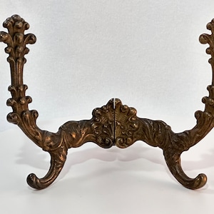 May include: A decorative metal stand with a scrolled design and two hooks. The stand is made of a dark bronze color.