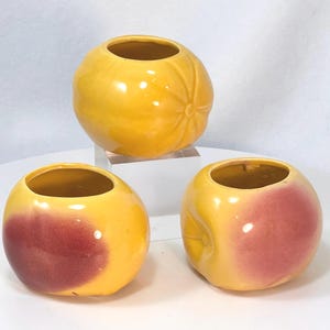 May include: Three ceramic decorative vases. Two are yellow with a red blush, and one is solid yellow. The vases are round with a small opening at the top. The solid yellow vase has a textured surface.