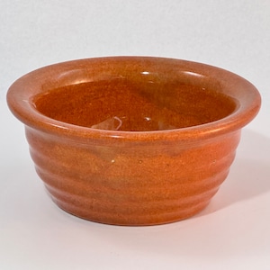 May include: A small, terracotta-colored ceramic bowl with a slightly rippled texture. The bowl has a smooth, glazed interior.