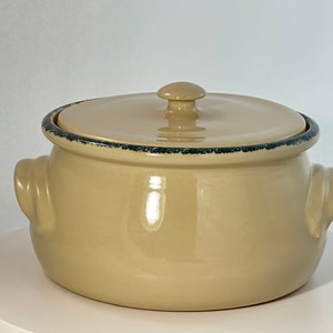 May include: A beige ceramic casserole dish with a lid and two handles. The dish has a dark blue rim around the top.