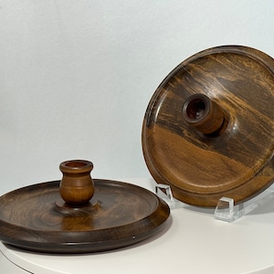 May include: Two wooden candle holders with a dark brown finish. The holders have a round base and a raised center for holding a candle.