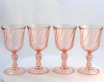 May include: Four pink-tinted glass goblets. Each goblet features a spiral design on the bowl, a stem, and a circular base. The glasses are arranged in a row, showcasing their elegant design and color.