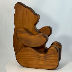 May include: A wooden bear figurine, carved from a single piece of wood, with a brown stain finish. The bear is sitting with its arms crossed and has a simple, stylized design.