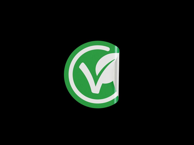 May include: A green circle sticker with a white checkmark and a leaf inside. The sticker has a white border and is peeling off at the top.