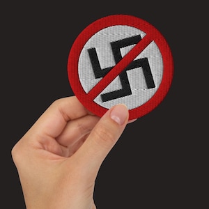 Puede incluir: Un círculo rojo con una línea diagonal que lo atraviesa, prohibiendo una esvástica negra sobre fondo blanco.