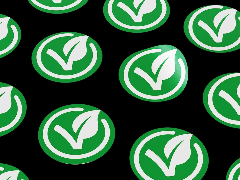 May include: A pattern of green and white circular stickers with a leaf and checkmark design. The stickers are on a black background.