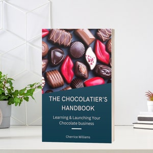 May include: A book titled "THE CHOCOLATIER'S HANDBOOK" with a cover showing various chocolates. The cover also includes the text "Learning & Launching Your Chocolate business" and the author's name, Cherrice Williams.