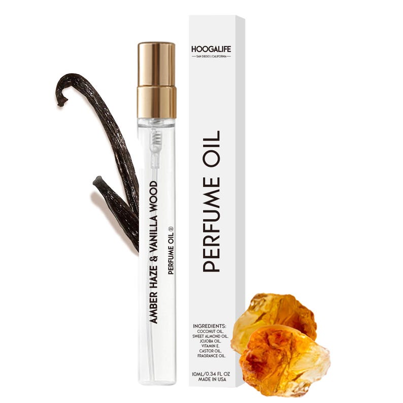 Op de afbeelding: Een heldere glazen fles met amber en vanillehout parfum olie met een gouden dop. De fles is gelabeld met de naam van de geur en de merknaam "Hoogalife". De fles staat op een witte achtergrond met een vanilleboon en barnsteenstenen.