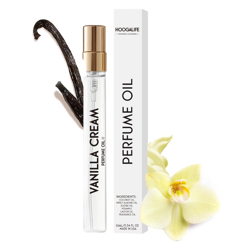 Op de afbeelding: Een klein, doorzichtig glazen flesje met een gouden dop en een etiket met de tekst "Vanilla Cream Perfume Oil". Het flesje staat op een witte achtergrond met een vanilleboon en een witte bloem.