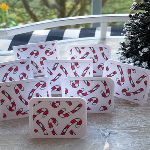 May include: Eight white cards with rounded corners, each featuring a red and white candy cane pattern. The cards are arranged in a staggered pattern on a light wood surface.