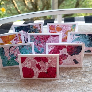 May include: Set of eight blank greeting cards with abstract floral designs in shades of pink, blue, yellow, and green. The cards are printed on white cardstock and have a textured finish.
