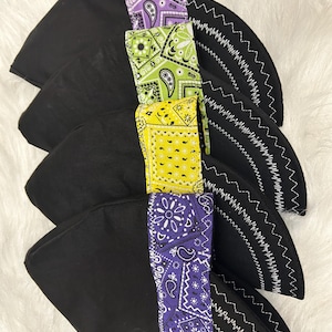 May include: A stack of four black skull caps, each featuring a distinct band of colorful bandana-print fabric. The bands are colored in light purple, lime green, bright yellow, and dark purple, all finished with white zigzag stitching.