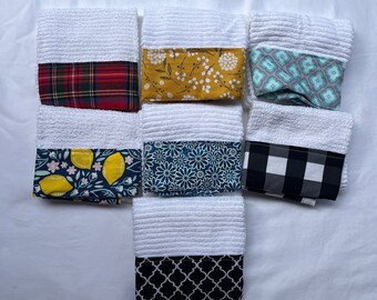 May include: Set of eight white kitchen towels with different colored and patterned fabric accents. The towels feature a variety of patterns, including plaid, floral, geometric, and lemon designs.