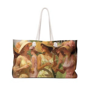 Op de afbeelding: Een witte canvas tote bag met een kleurrijk beeld van vijf vrouwen die hoeden en jurken dragen en glazen wijn vasthouden. De vrouwen lachen en lijken plezier te hebben op een sociale bijeenkomst.