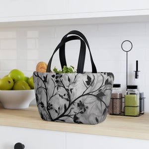 May include: A black and grey tote bag with a floral pattern. The bag has black handles and is sitting on a wooden counter.