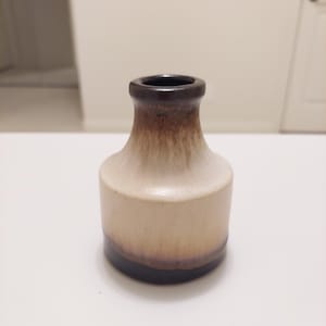 May include: A small, brown and white ceramic vase with a rounded body and a narrow opening. The vase has a brown glaze on the top and bottom, with a white glaze in the middle.