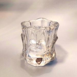 May include: A clear glass candle holder with a textured, ribbed design. The holder has a small, brown label on the bottom that reads "Orrefors Sweden".